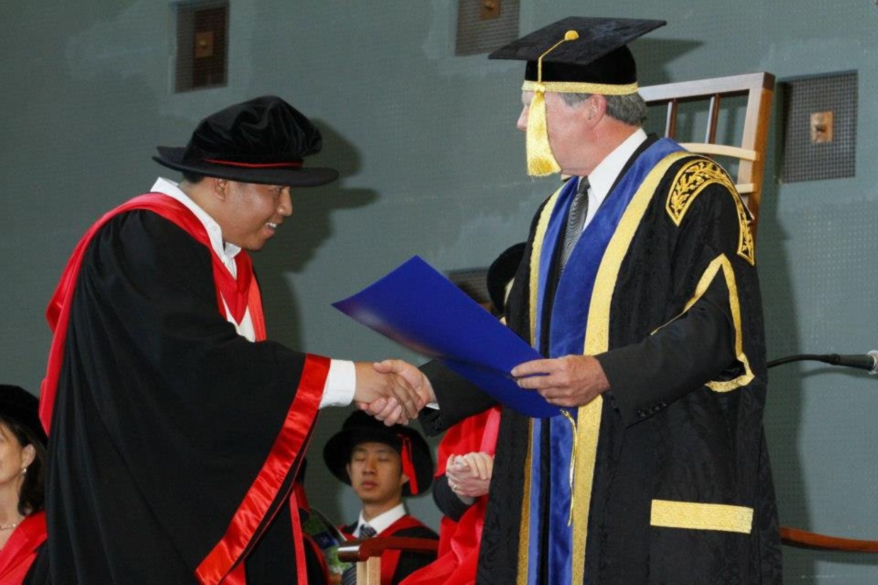 A man wearing robes shaking hands with another man while receiving a certificate