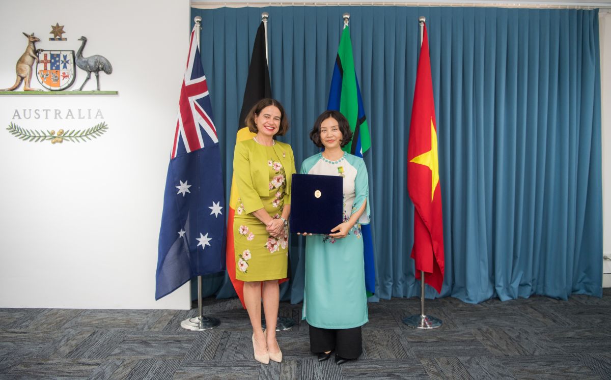Two people stand together holding a certificate in front of the flags of Australia and Vietnam.