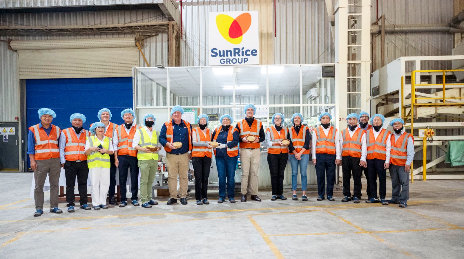 Group of visitors in safety gear standing inside a SunRice Group facility.
