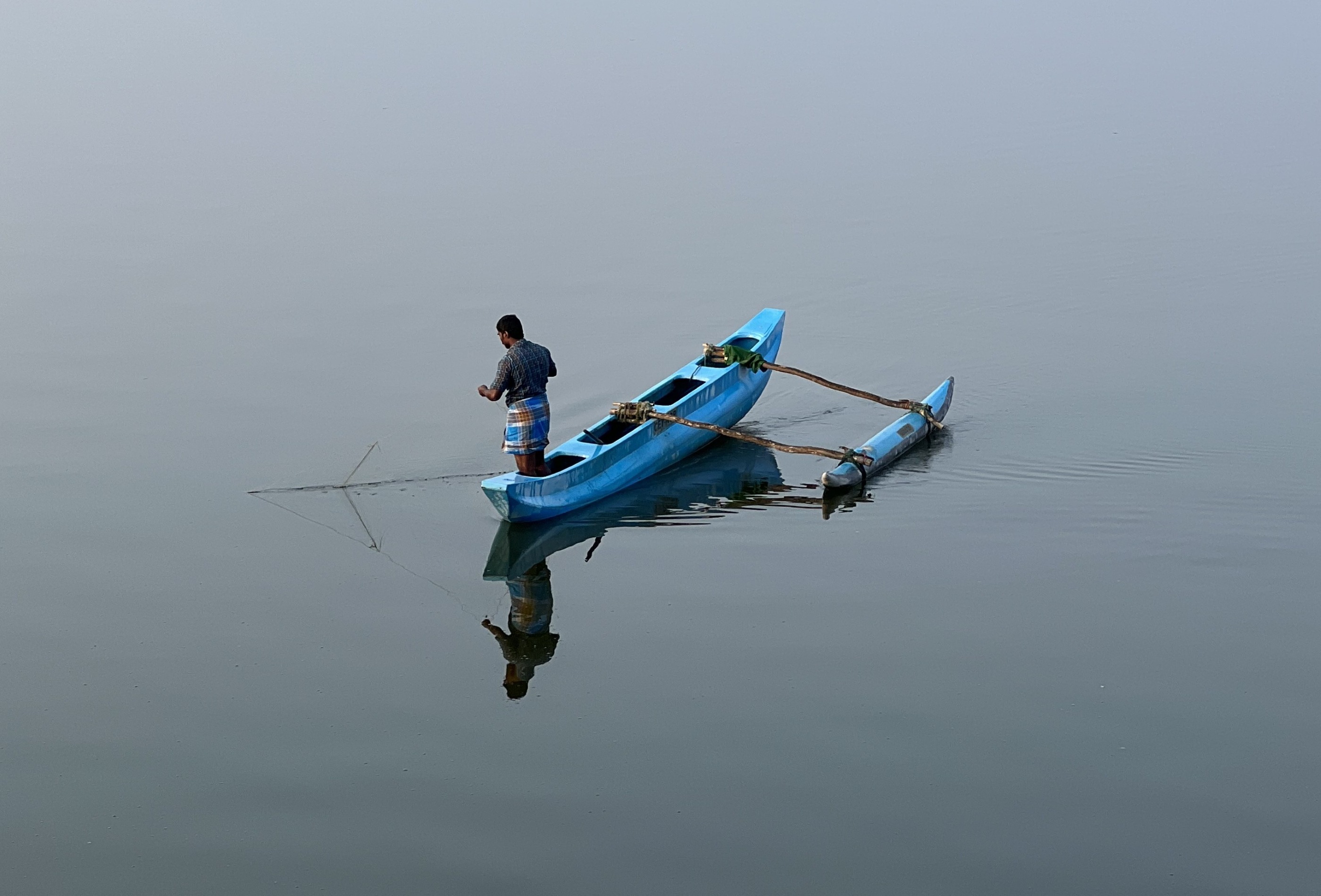 Person fishing from a narrow blue canoe on a quiet lake.