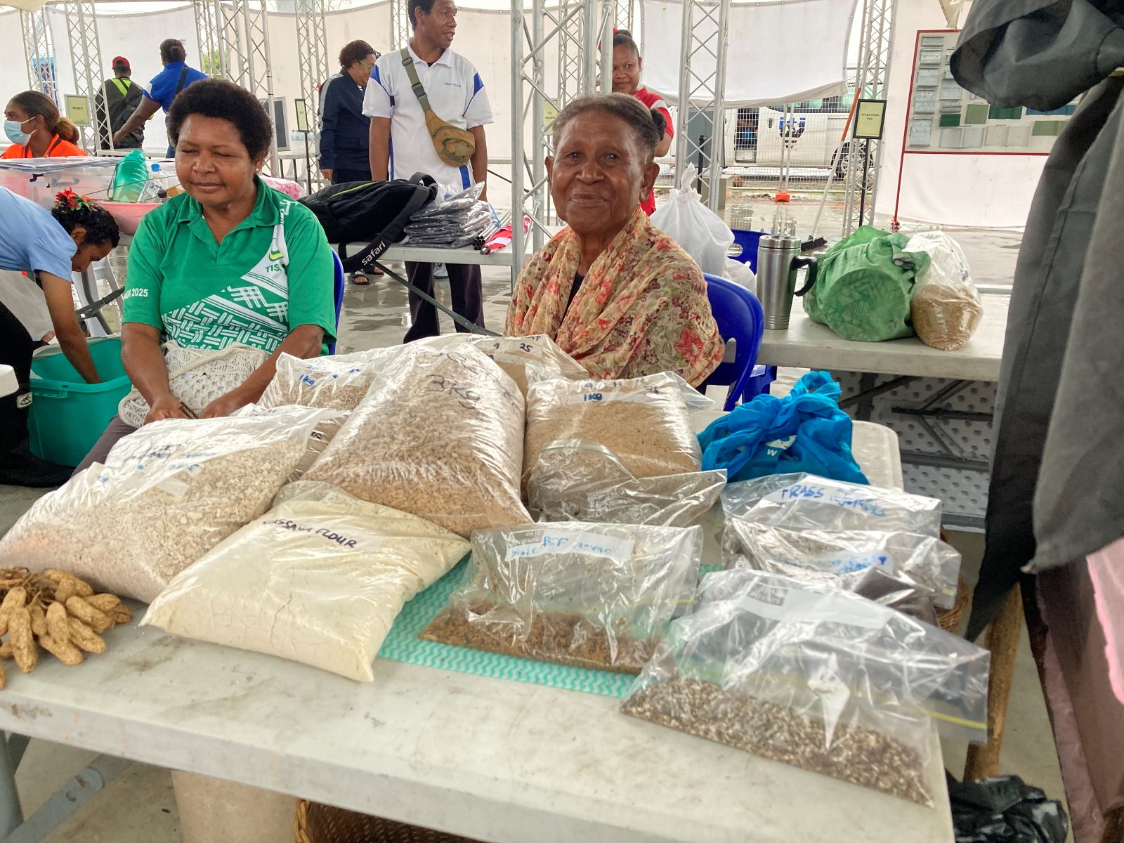 Two people seated behind a table of labelled grain and seed samples.