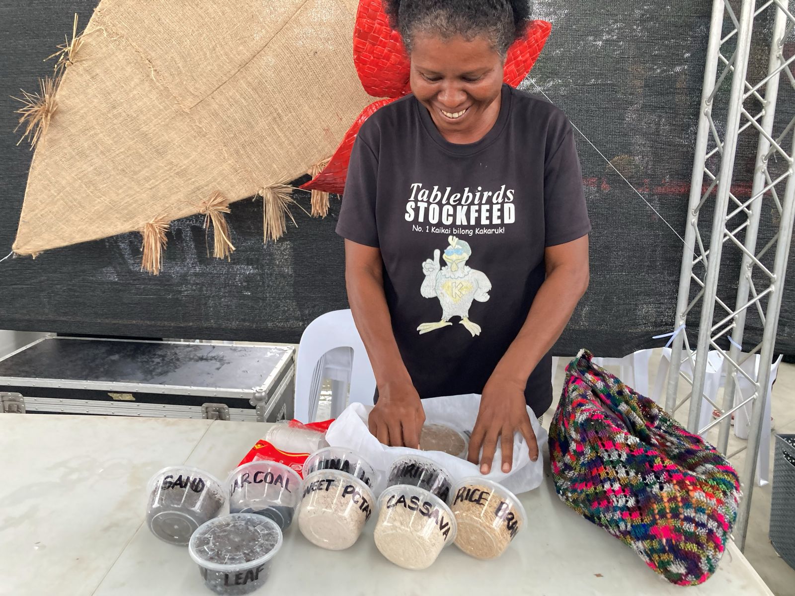Person standing behind a table displaying labelled stockfeed ingredients in containers.