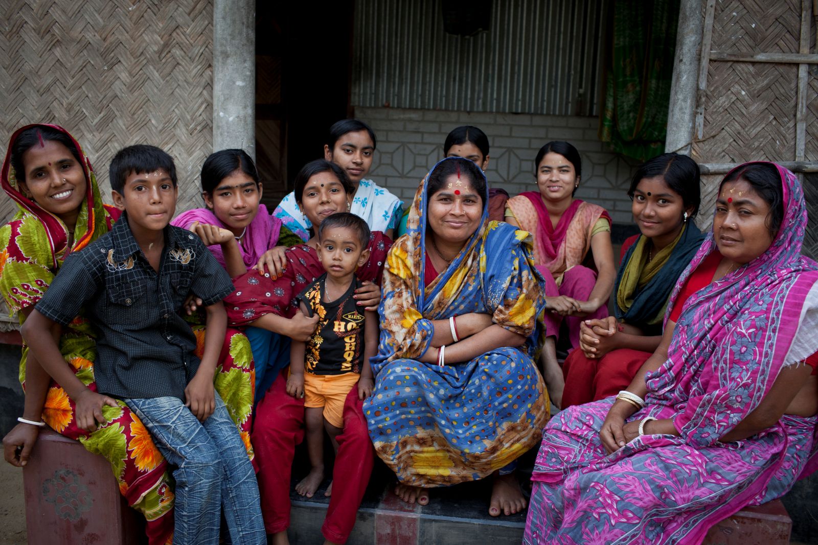Small group gathered on steps outside a woven‑wall house.