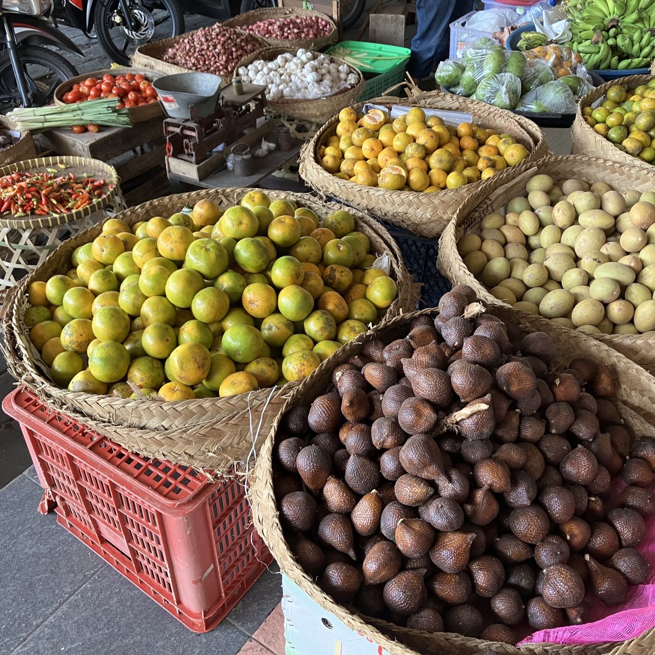 Market stall displaying baskets of fresh fruit and vegetables, including citrus, potatoes and chillies.
