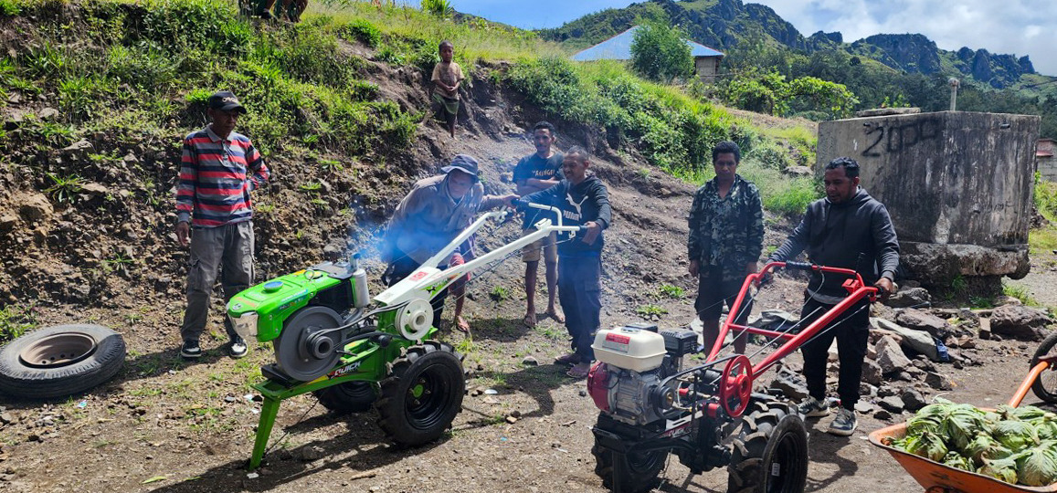 Farmers operate hand-held machinery on a hillside, demonstrating small-scale agricultural equipment.