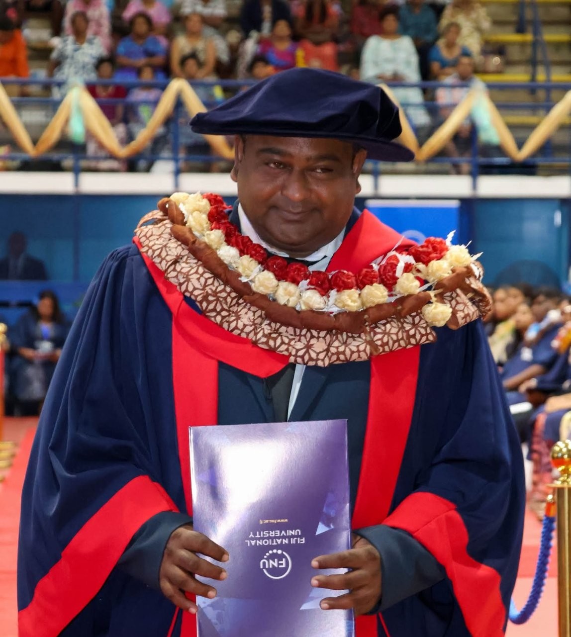 Graduate in academic regalia holding a degree certificate during a university graduation ceremony.