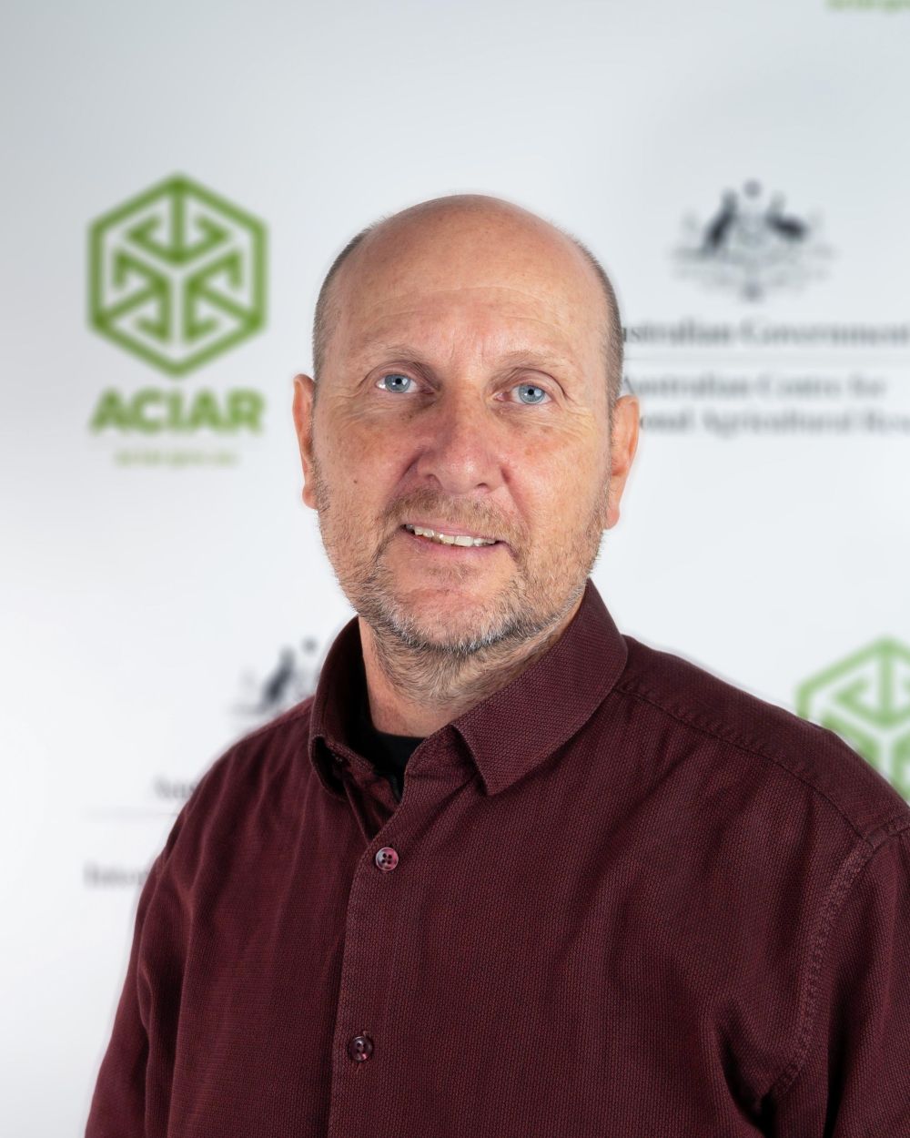 Bio headshot image of Dr Nick Harris standing in front of ACIAR banner