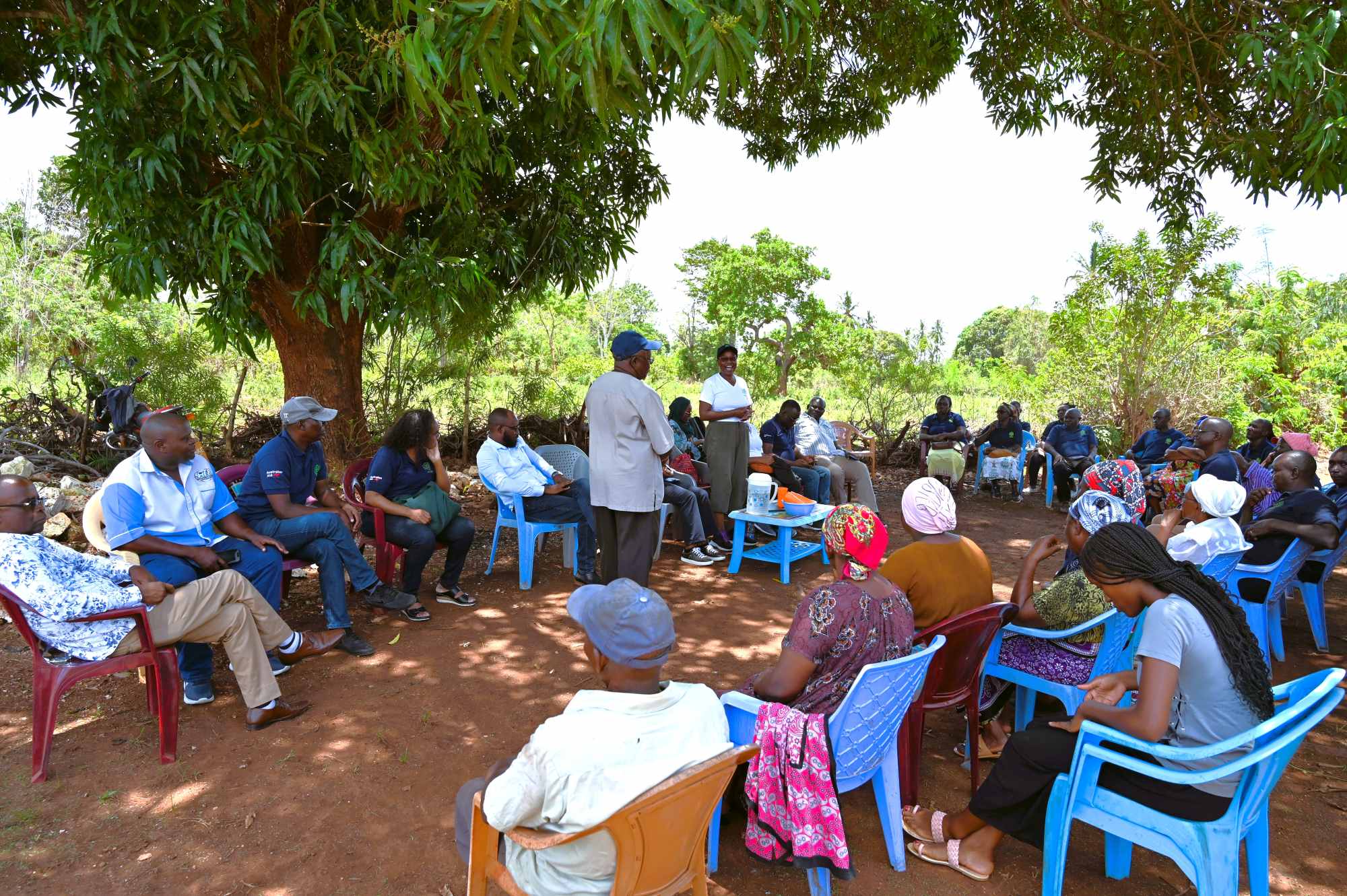 Community members gathered outdoors for a training and discussion session under trees.