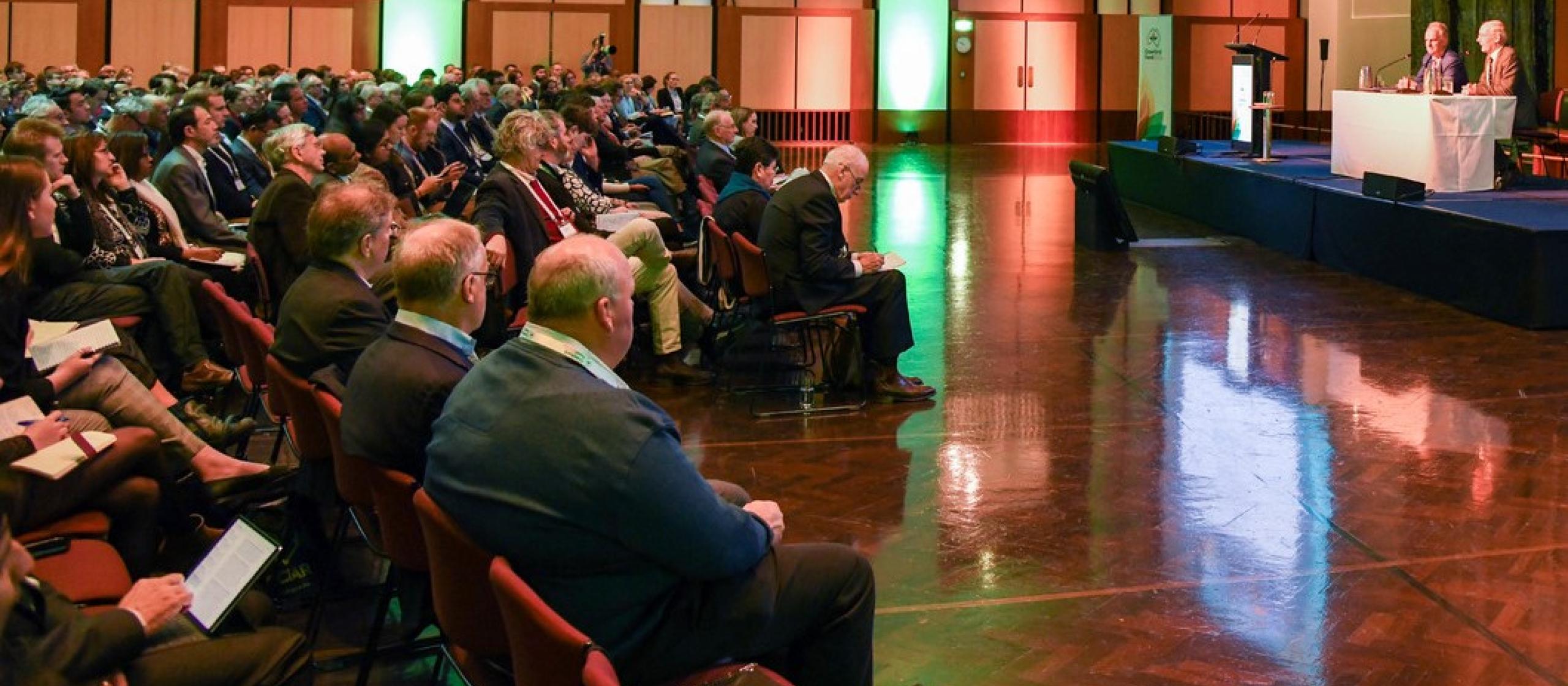 a large room full of people with 2 speakers at the front 