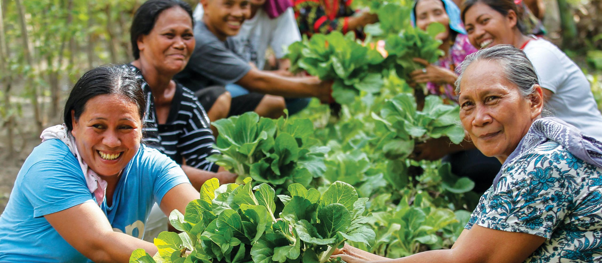 women farmers smiling seated within a crop of fresh green vegetables.