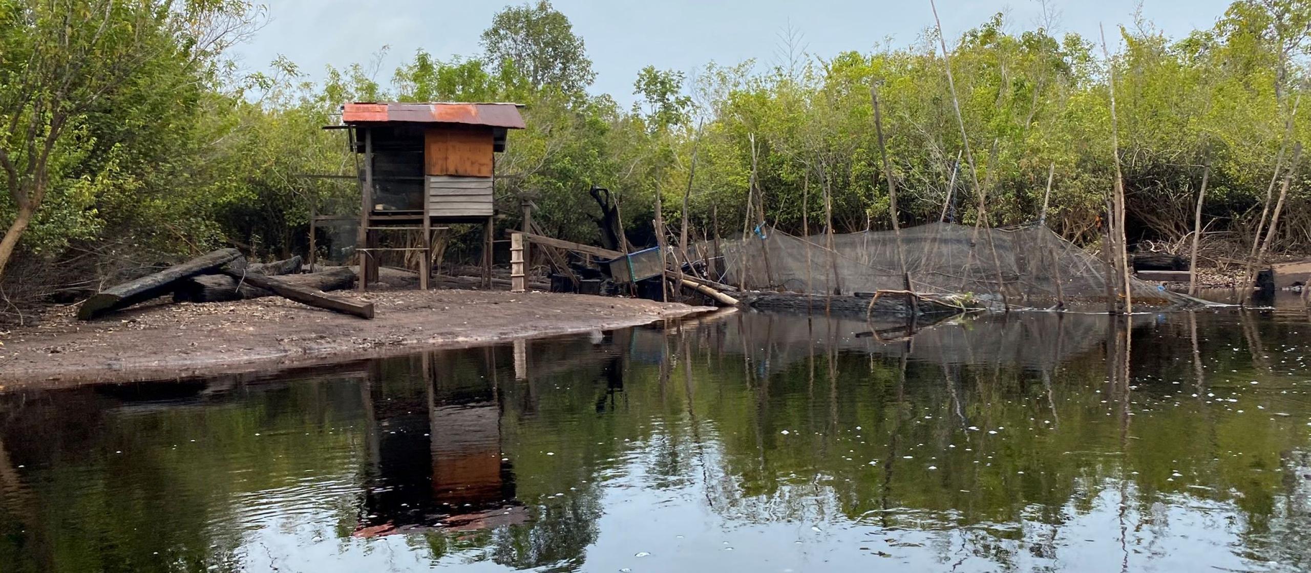 A small wooden hut sitting on a bank next to murky water