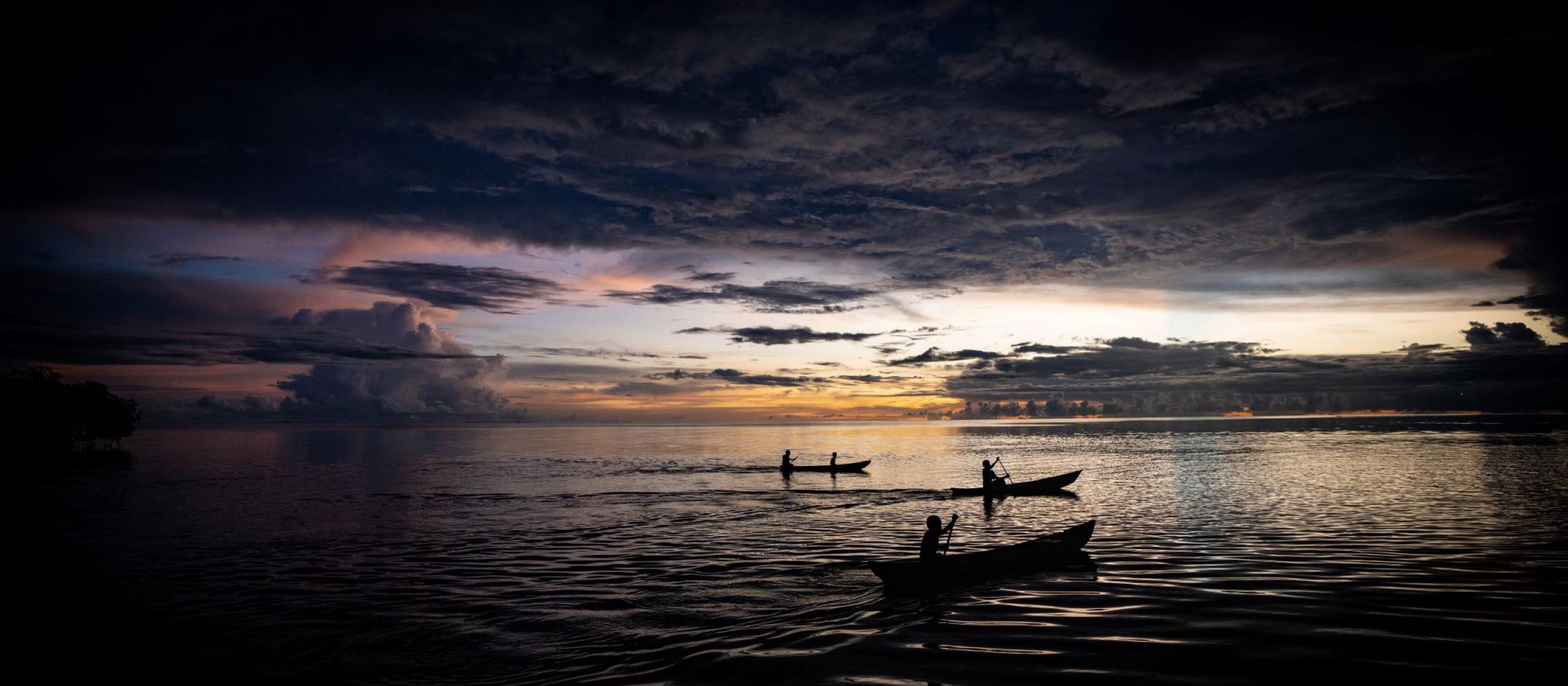 A group of people in canoes on the water at sunset