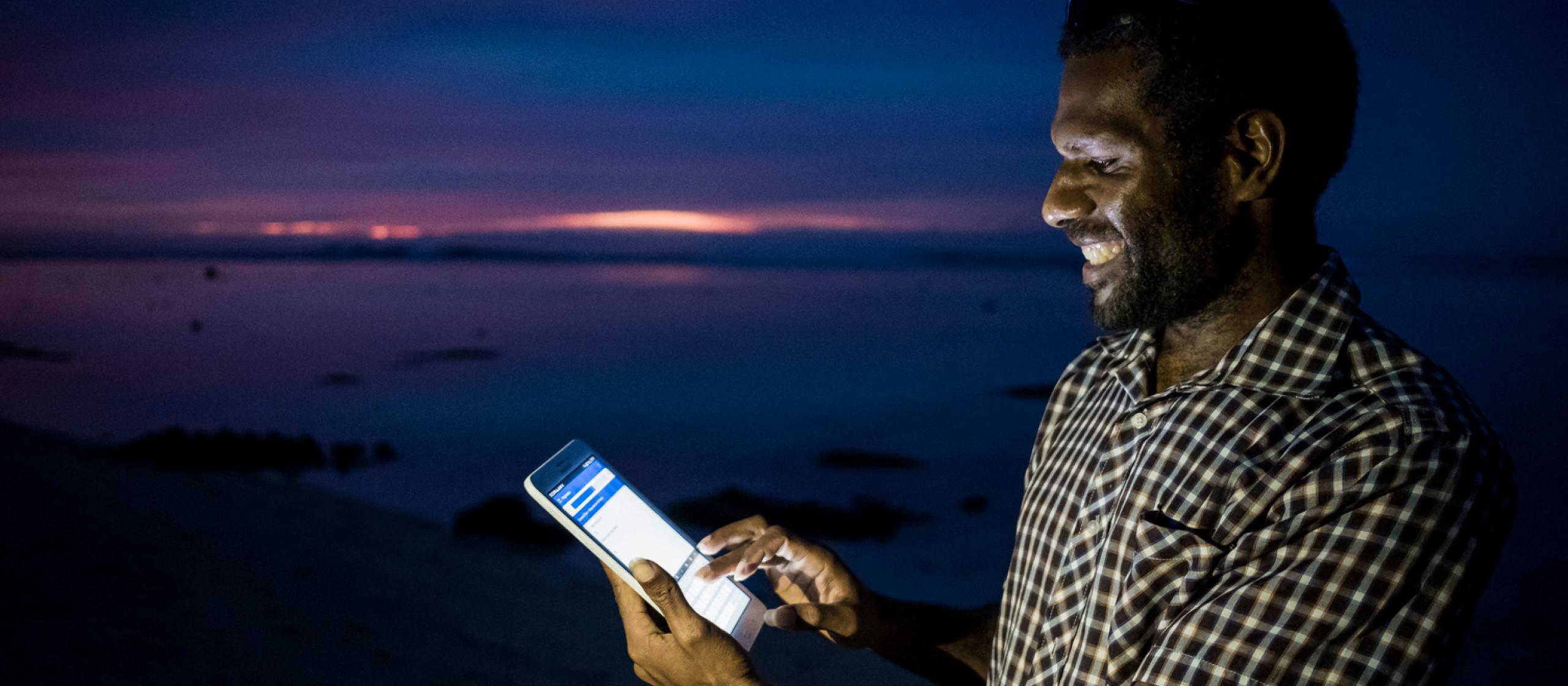 Male using a tablet with the screen glowing against the dark ocean backdrop.