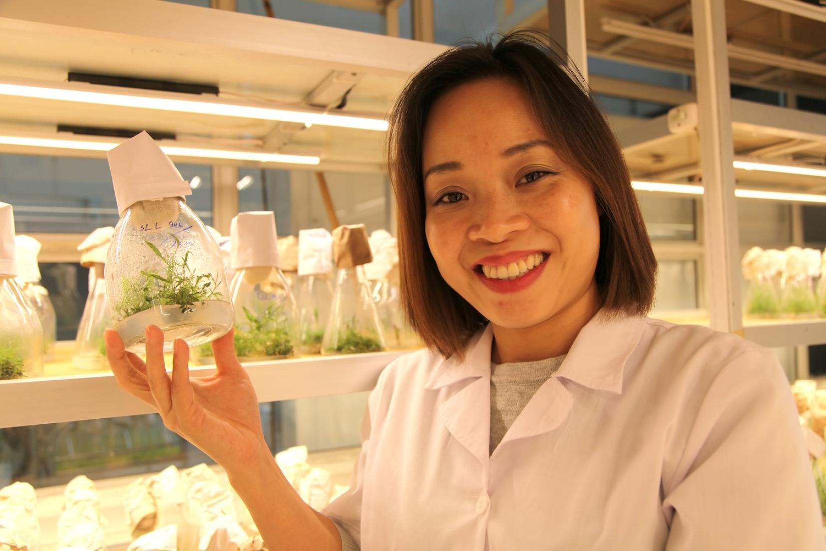 Female scientist holding up a plant in a glass bottle