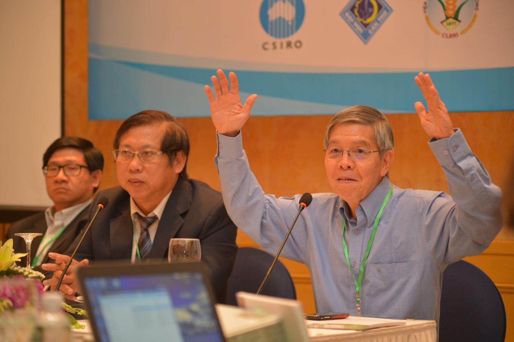 Three men in a conference room. One has both hands in the air