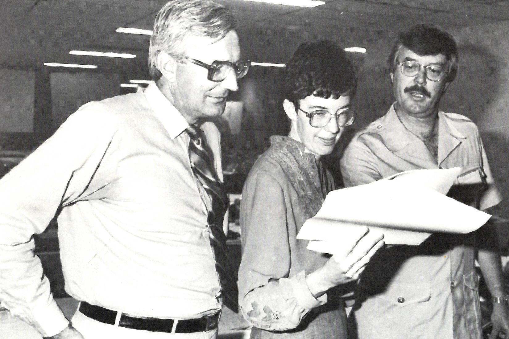 Black and white photo of woman and two men looking at a report