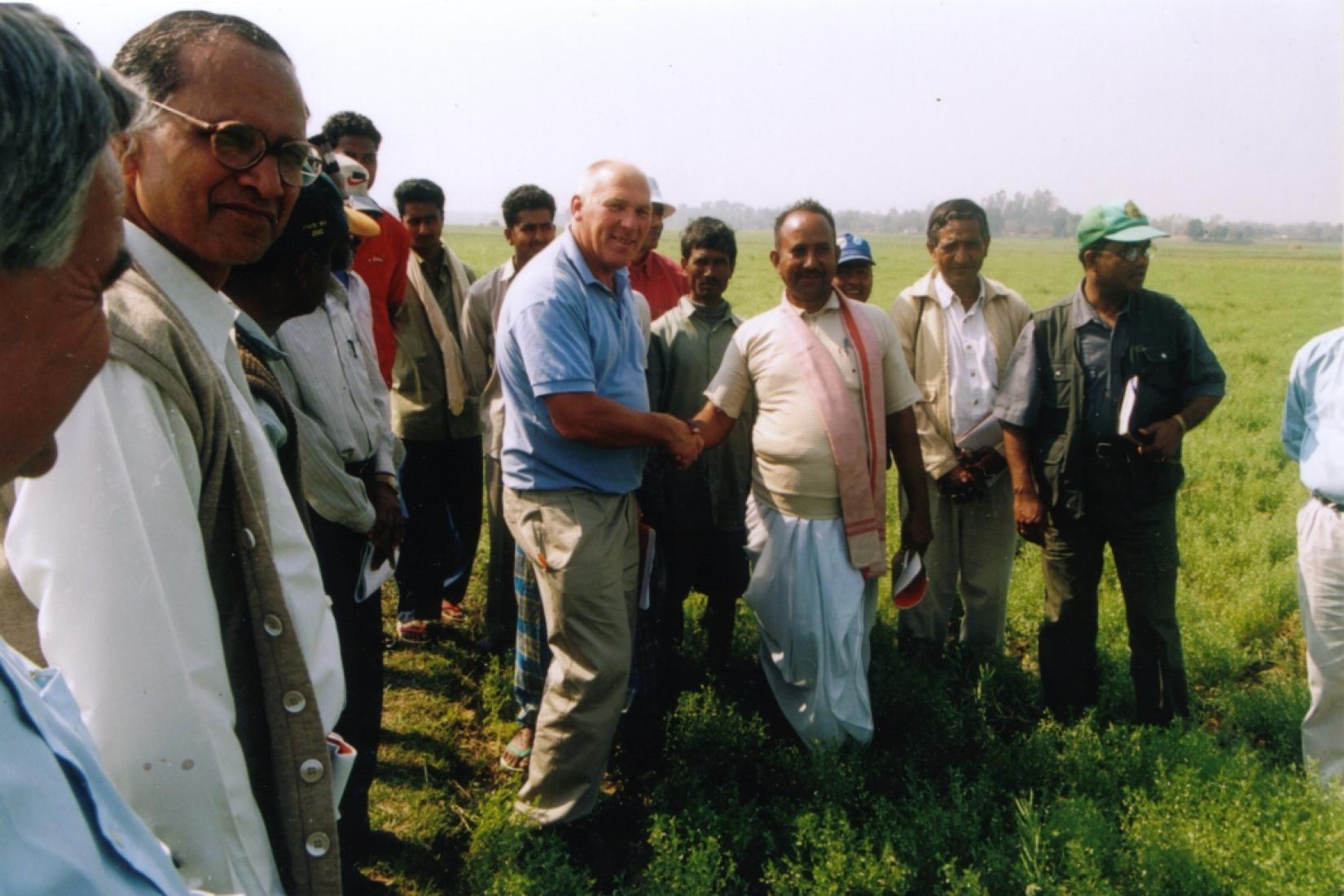 Men shaking hands in field with a group of men around them 