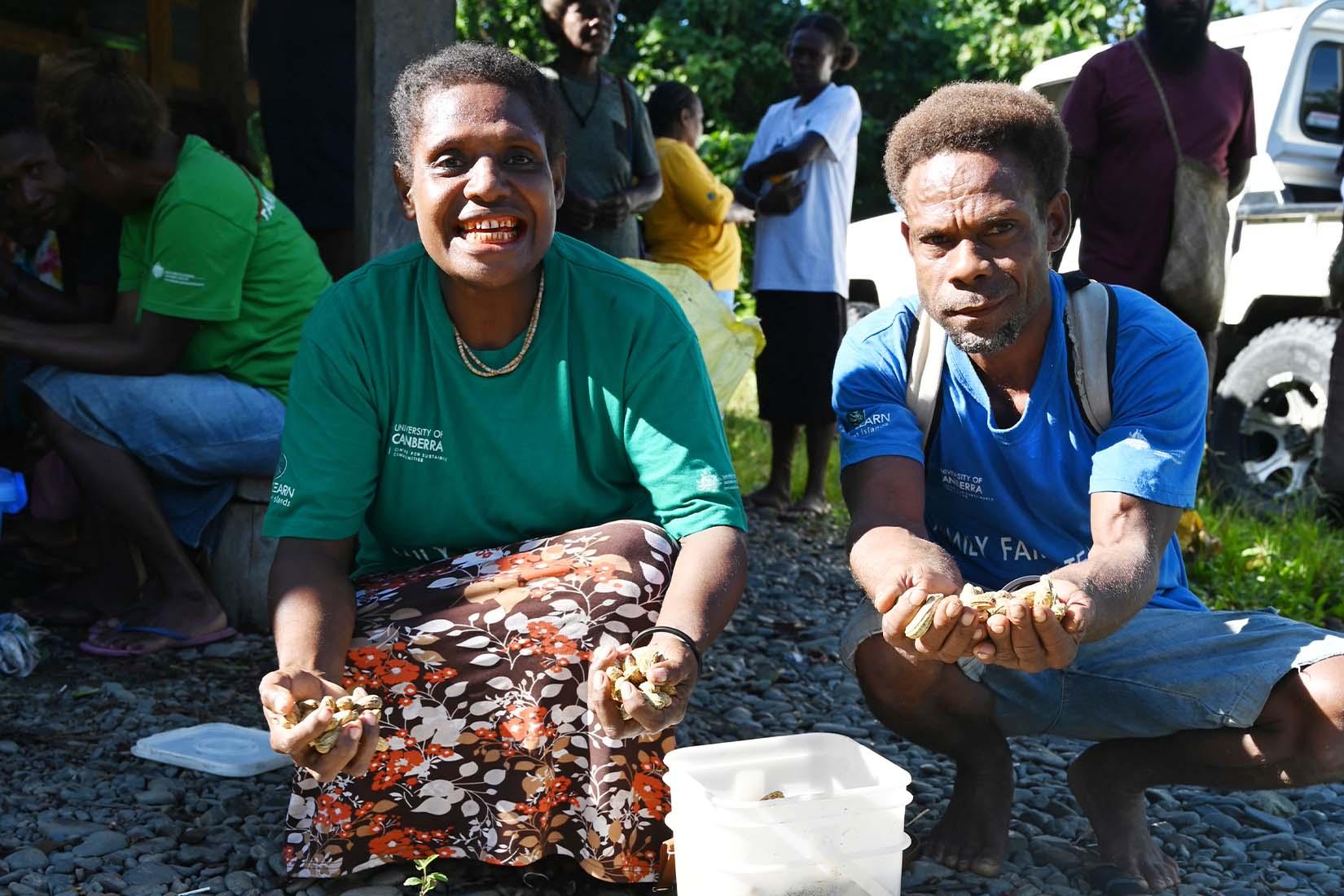 Two people smiling, holding out handfuls of peanuts towards the camera.