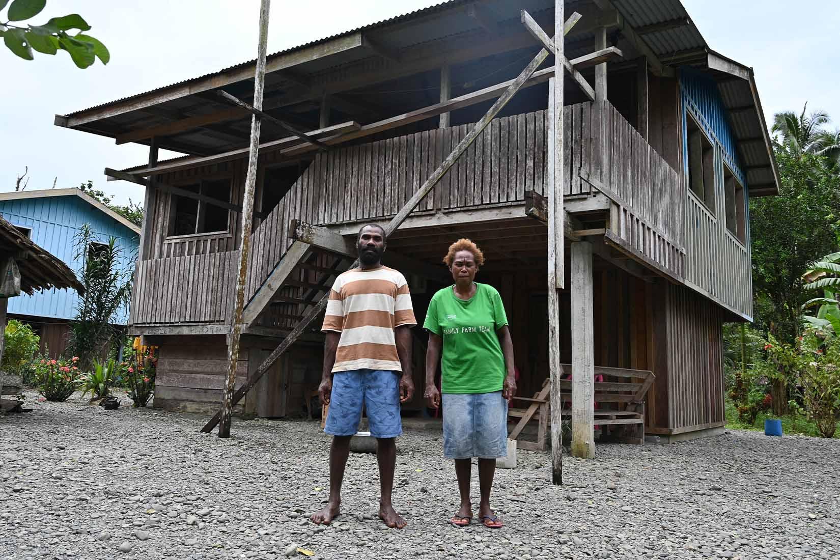 Two people standing in front of a 2 story house made of wood