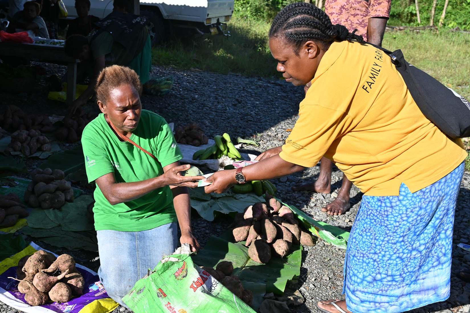 Two women in a market exchanging fresh produce