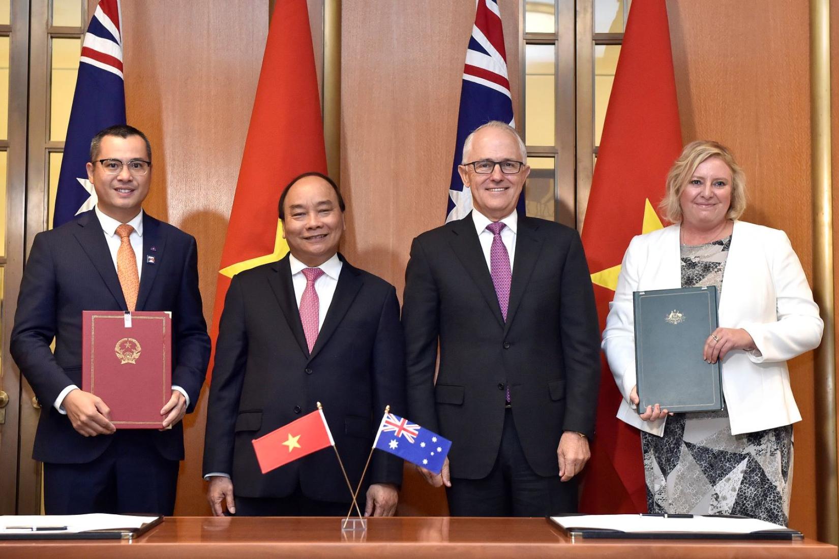 Four people standing with flags of Vietnam and Australia while displaying books with Vietnam and Australian crests