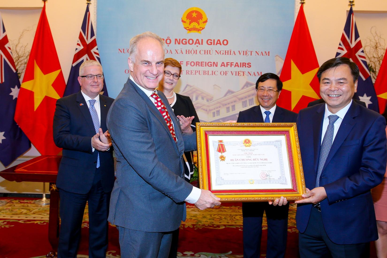 Men displaying a certificate with medal with Vietnam and Australian flags in background