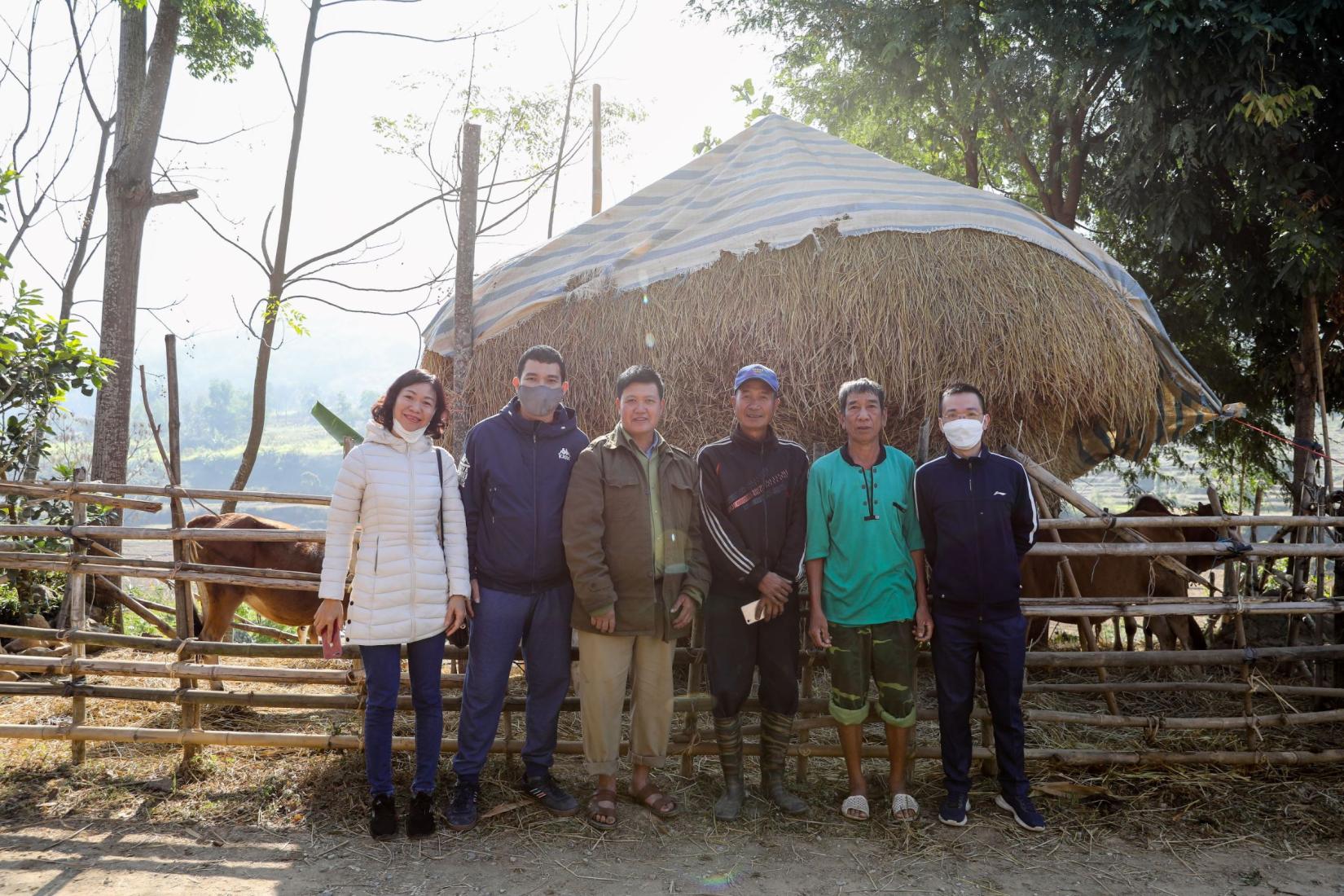 A group of people standing in front of a pen with animals and hay