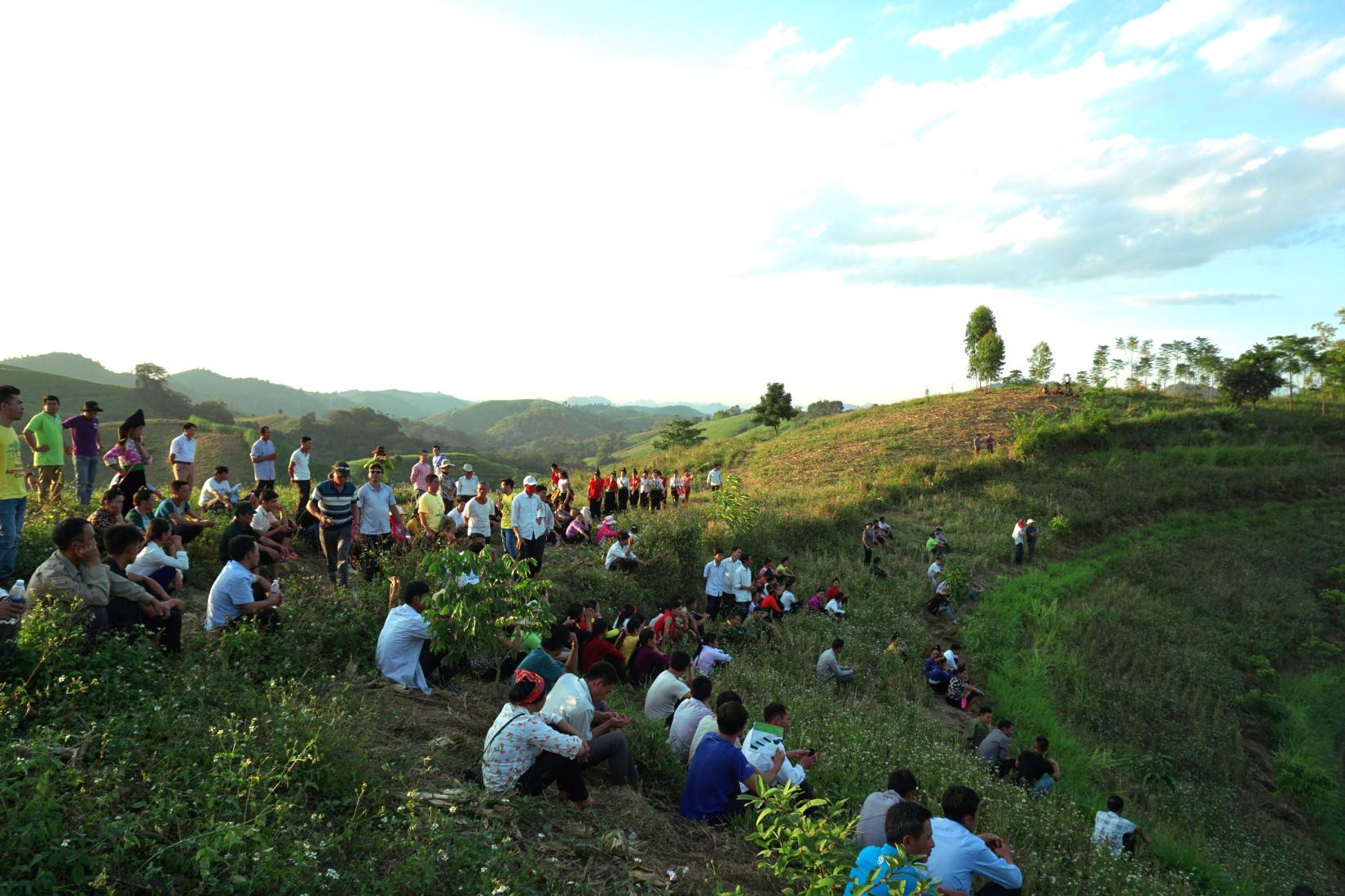 A group of people siting and standing looking out over a hillside