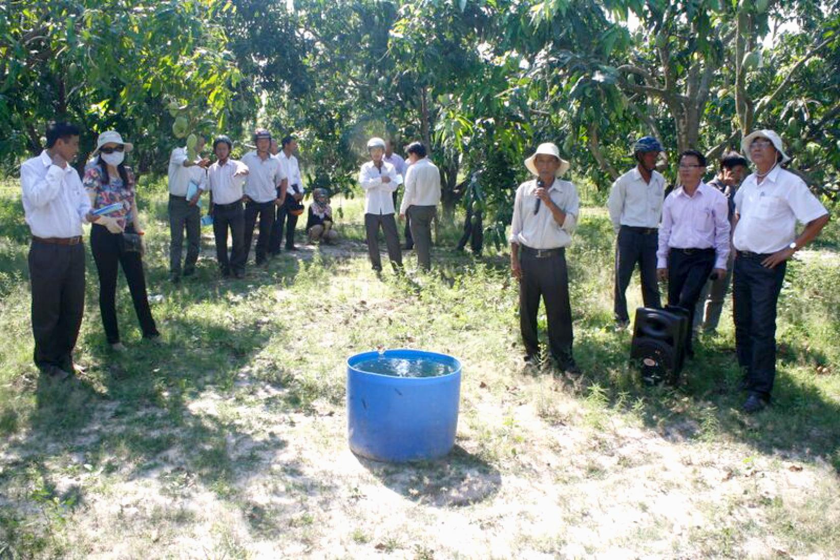 A group of people in a field looking a container of water for irrigation