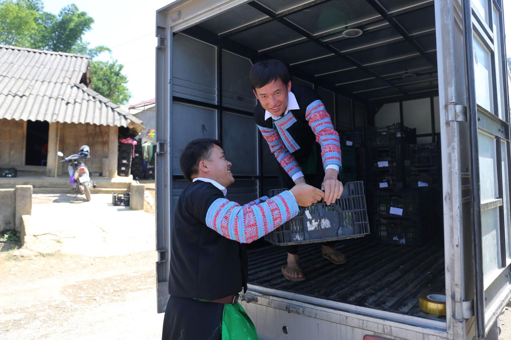 Two men smiling loading crates into a truck