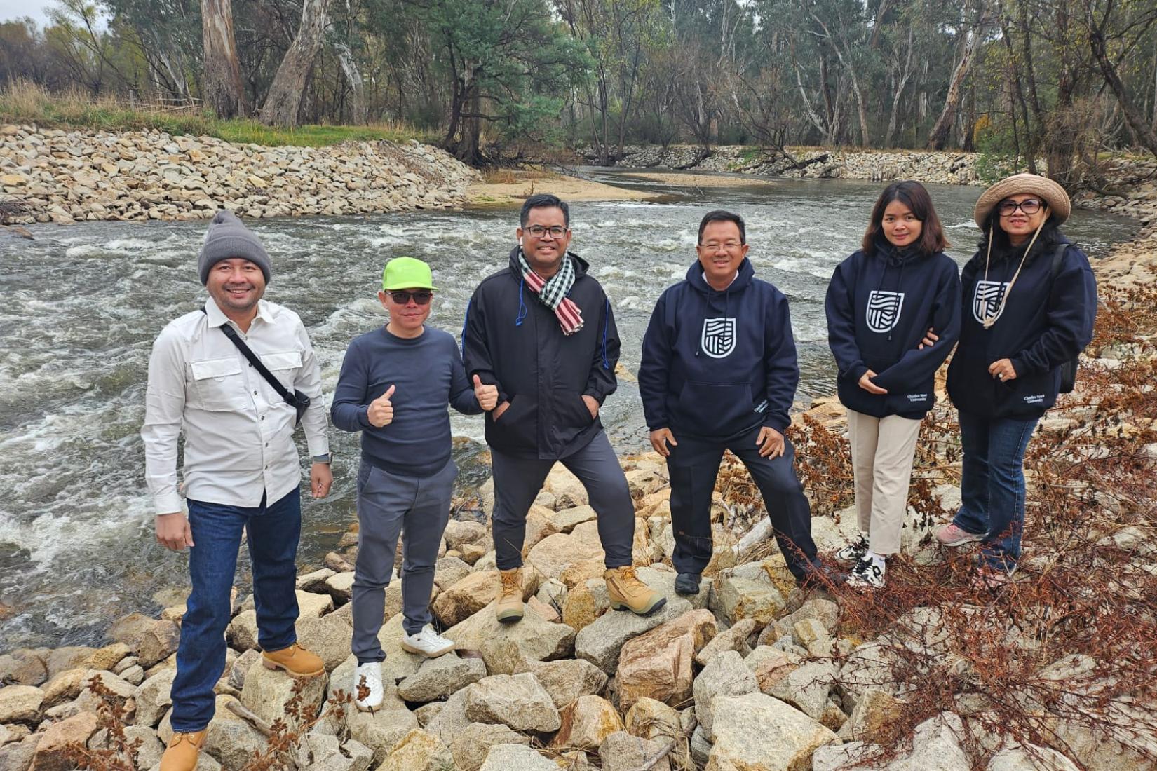A group of six people standing on a rock river bank with the river in the background