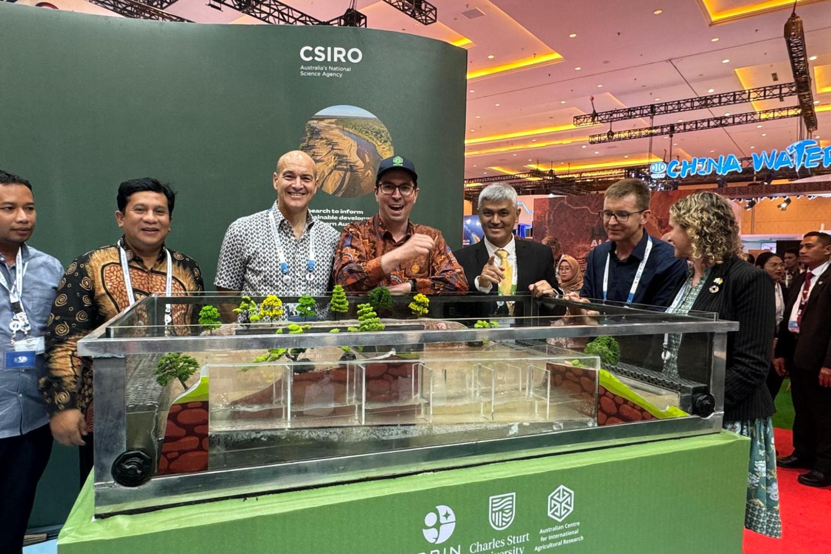 Group of 6 people standing behind a glass tank