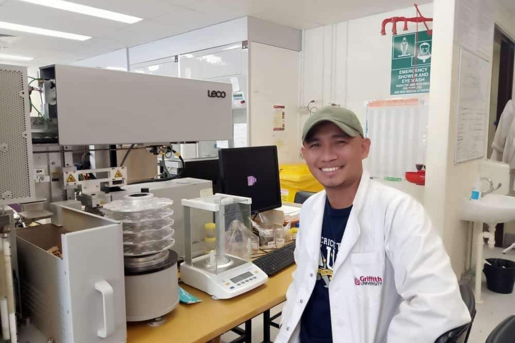 Man in white lab coat sitting at a desk of scientific equipment