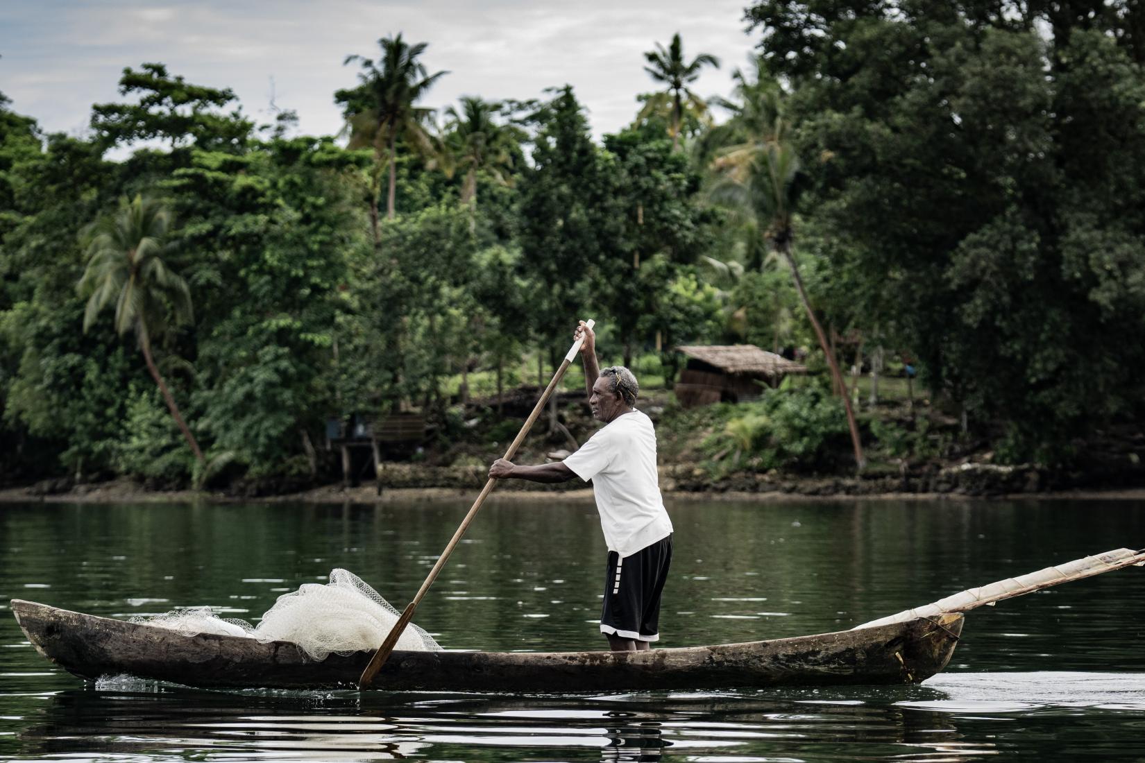 A man stands with a paddle and a fishing net in a wooden canoe