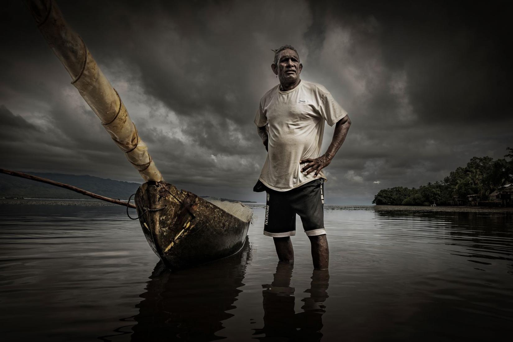 A man standing in ankle-deep water next to his canoe with his hands on his hips.