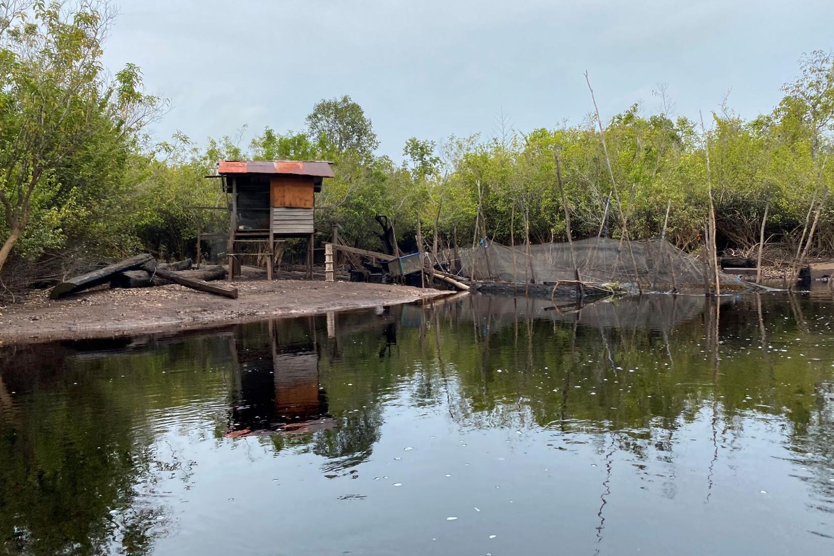A small wooden hut sitting on a bank next to murky water