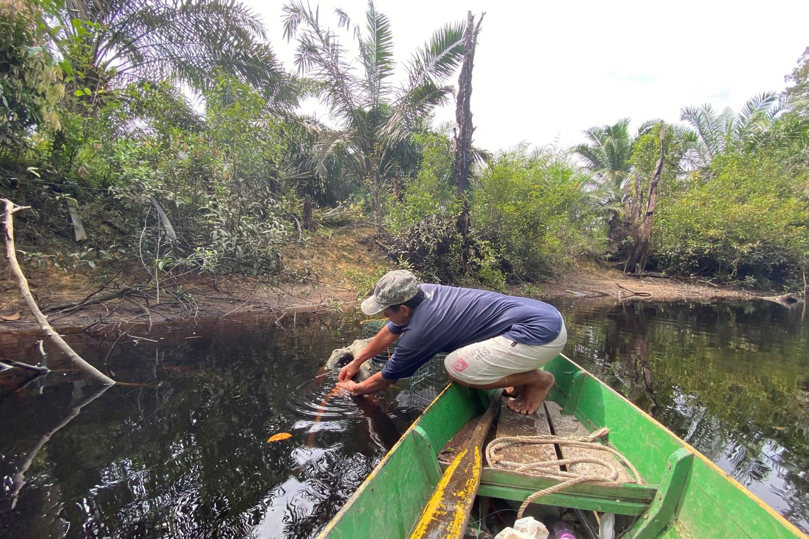 A man in a green boat working with a net in murky water