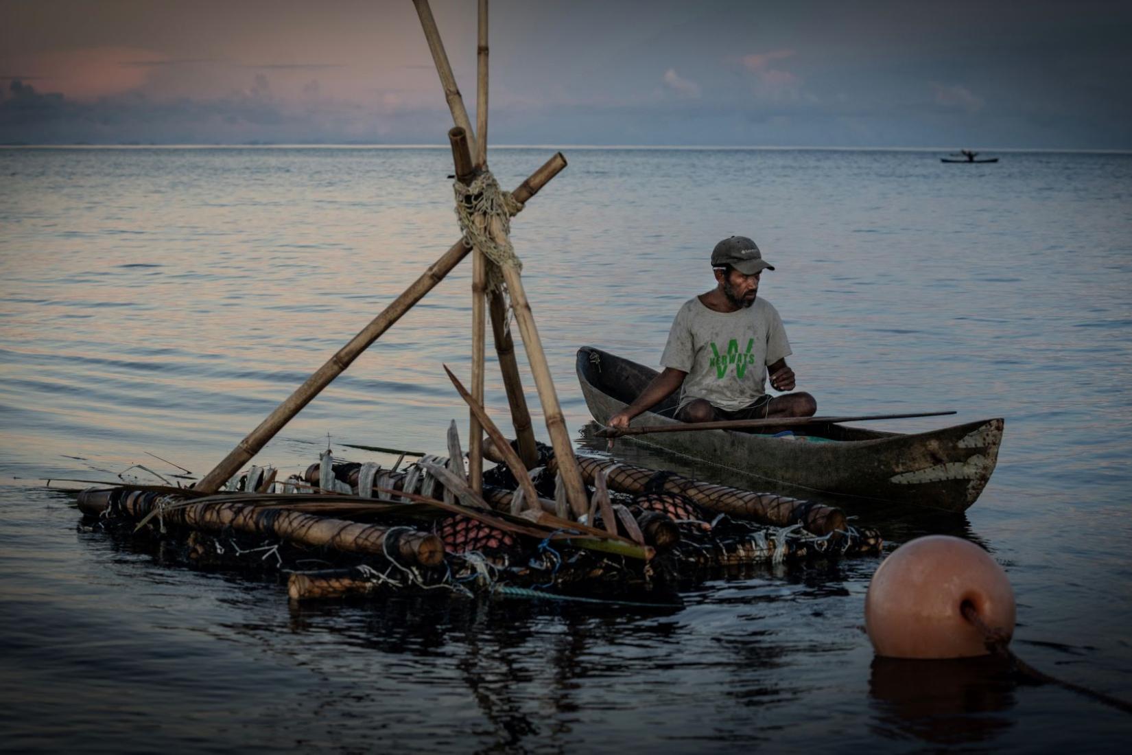 A person sitting in a canoe on the water next to a raft construction. 
