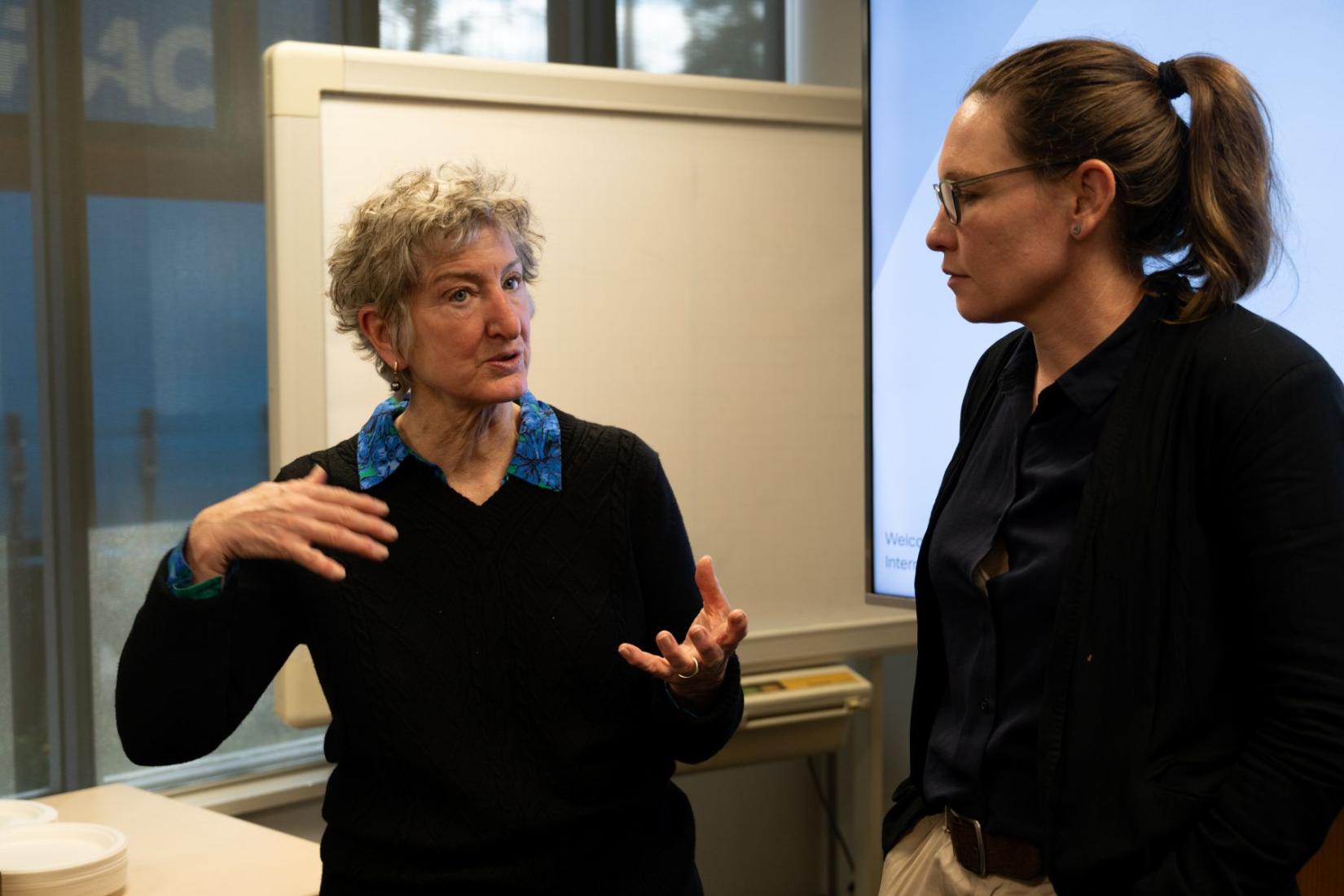 Nora devoe speaks to a colleague in front of a whiteboard.