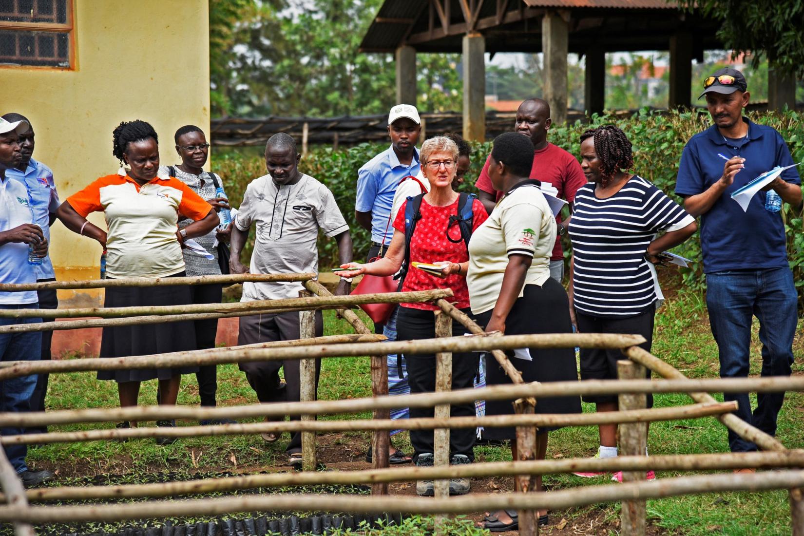 Nora Devoe speaks to a group of people outside standing in front of wooden structures.