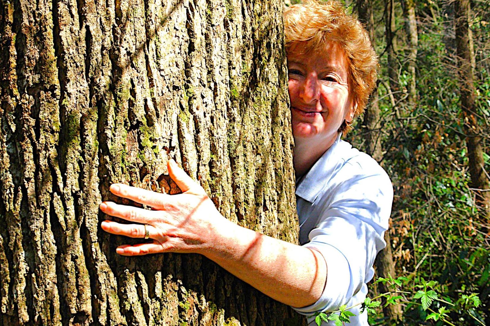 Nora Devoe with her arms wrapped around the trunk of a tree.