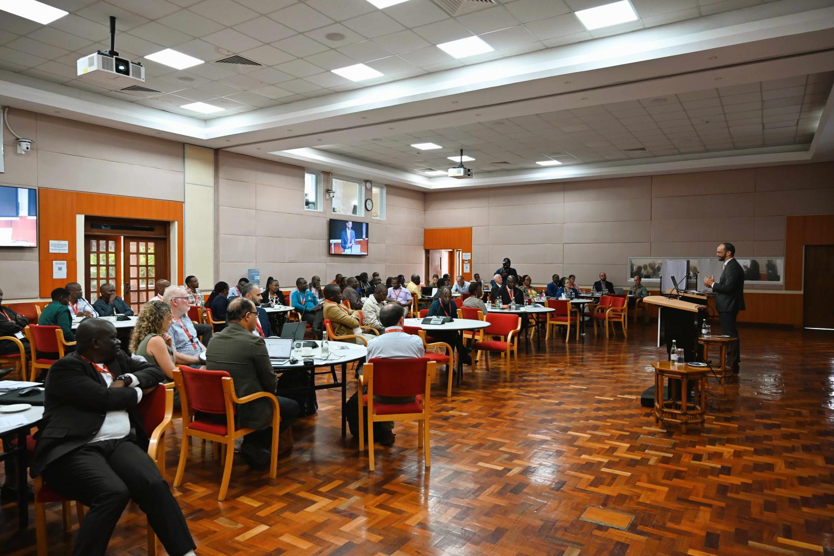 Workshop participants sitting around round tables listening to a speaker at the front of the room