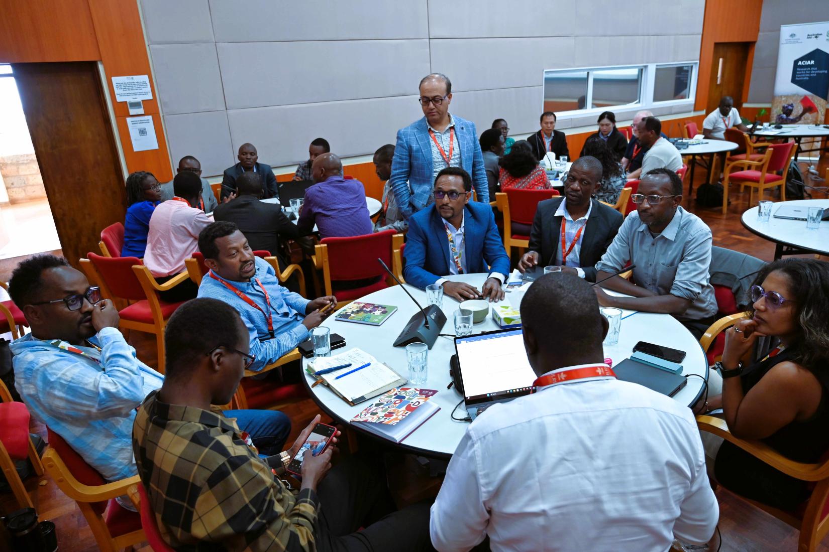 Small groups in discussion around tables during an indoor workshop.