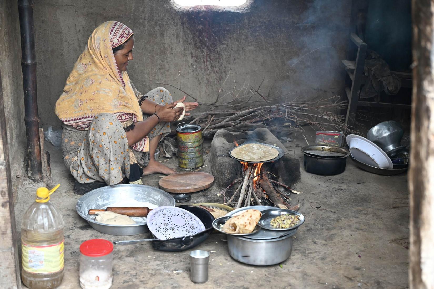 Person cooking flatbread over a wood-fired stove inside a home.