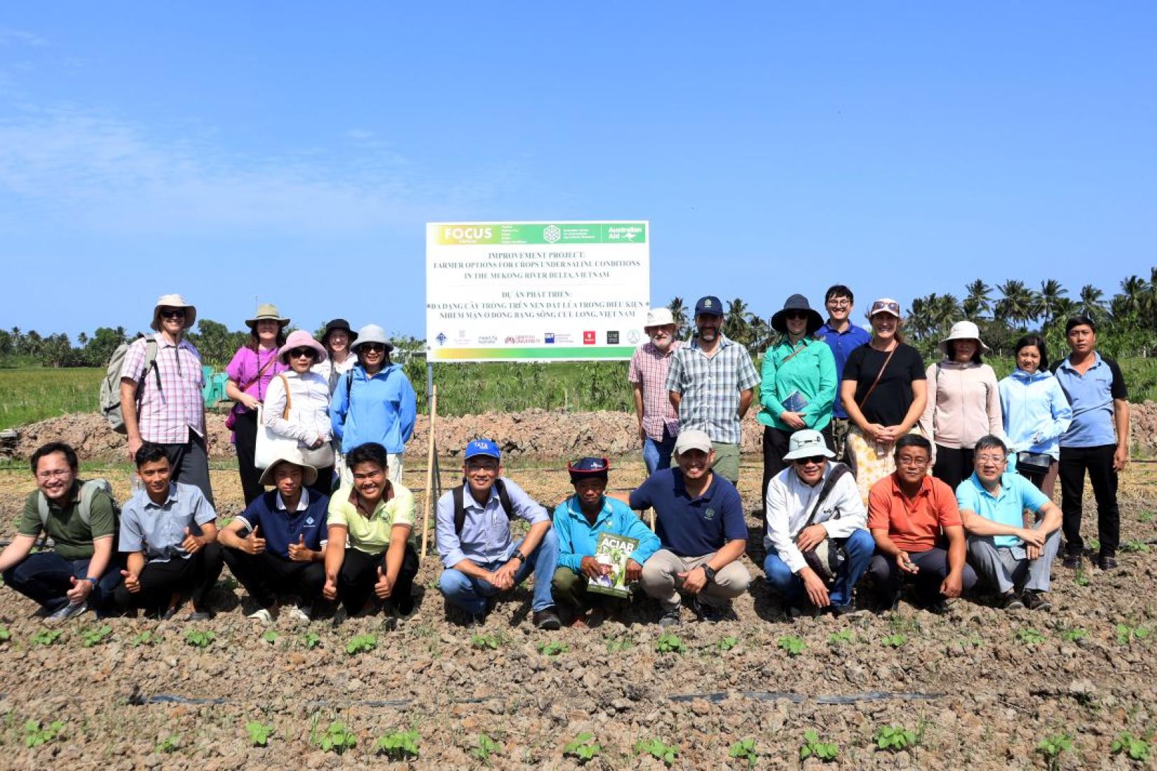 Group photo of farmers, researchers and project partners standing in a trial field beside a project information sign.