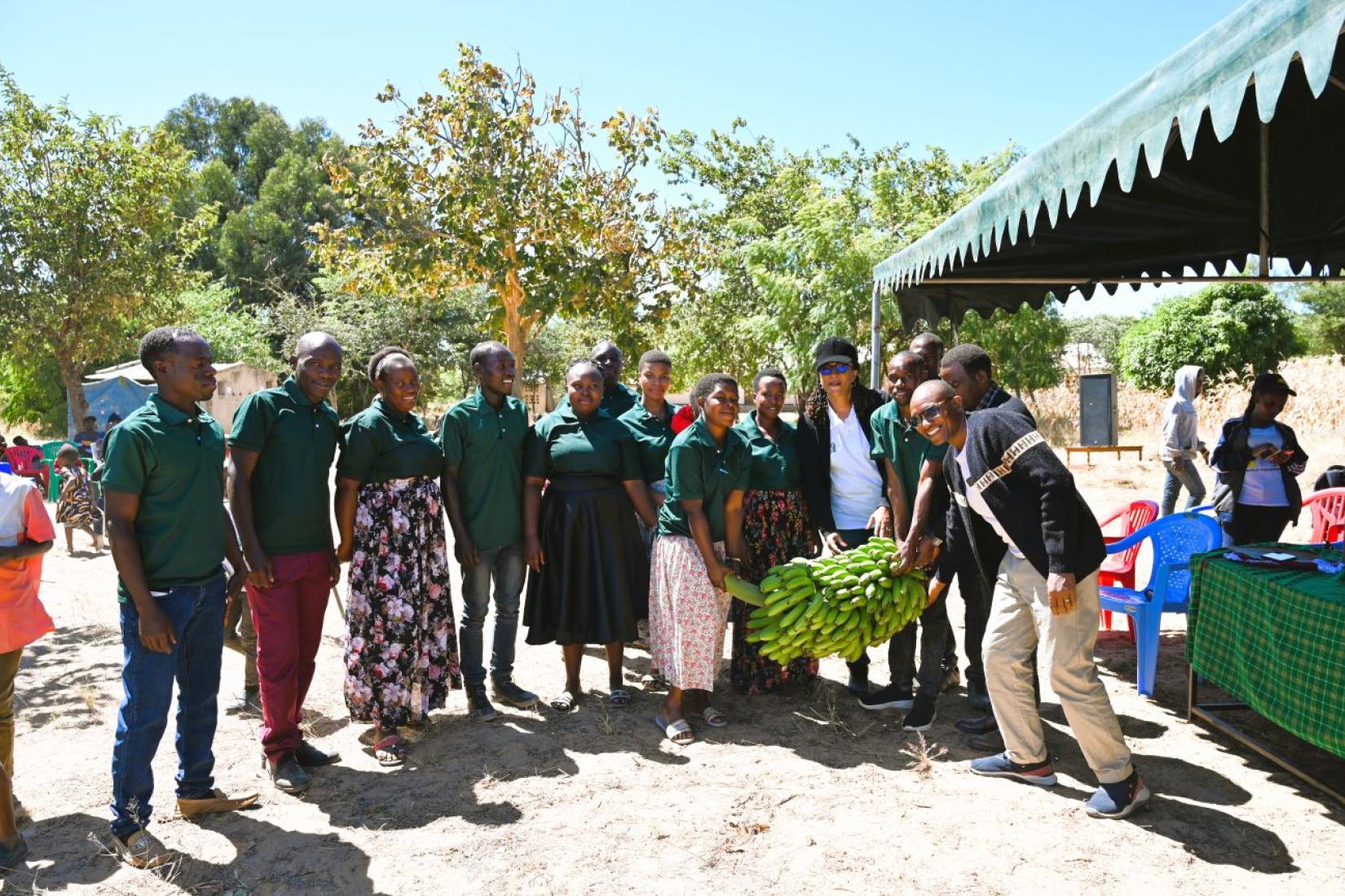 Group of people gathered outdoors around a large bunch of bananas.