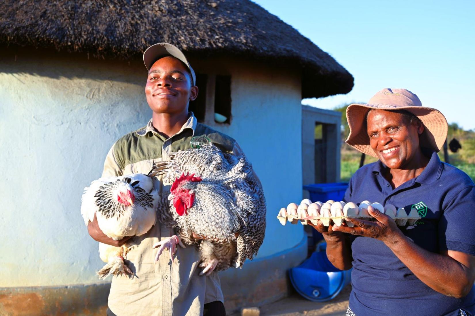 Two people holding chickens and a tray of eggs.
