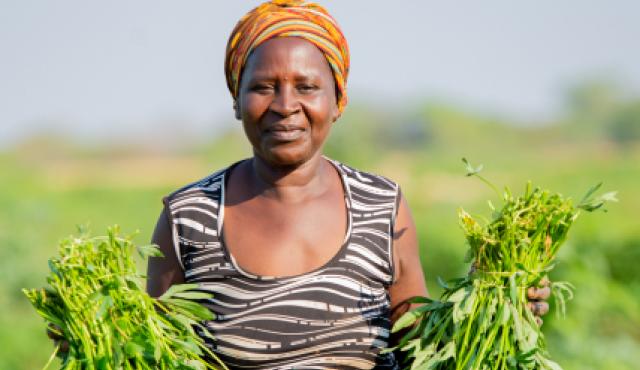 a woman smiles at the camera while holding green vegetables in each hand