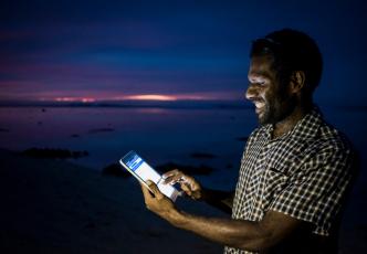 Male using a tablet with the screen glowing against the dark ocean backdrop.