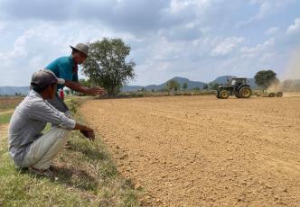 Two farmers observe a tractor levelling a field.